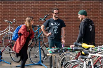 Three young people chatting and laughing at a bike workshop on campus.