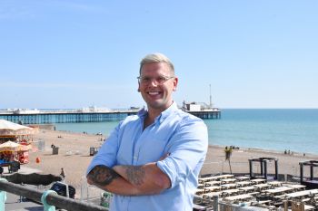 An image of Dr Duncan Shrewsbury stood with his arms folded next to the Brighton pier on the seafront