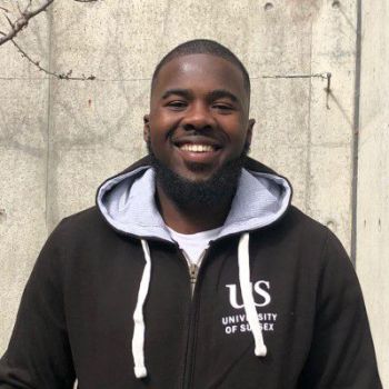 Student Ambassador Shaq Jarrett standing outside a University building in a grey Sussex hoodie.