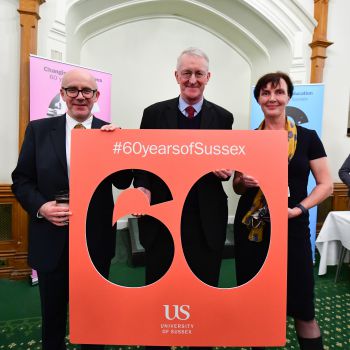 Two men and a woman face the camera holding a carboard cut-out of the number 60