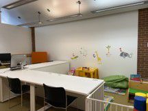 White desks arrange in an L shaped around a gated play area with colourful toys on the floor