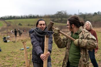 A student holds a large wooden stake as a staff volunteer raises a hammer to knock it into place