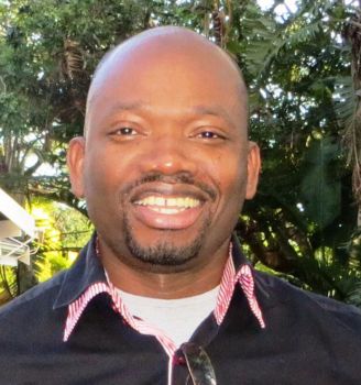 A photo showing Collins Iwuji, a researcher in HIV, smiling at the camera with trees in the background