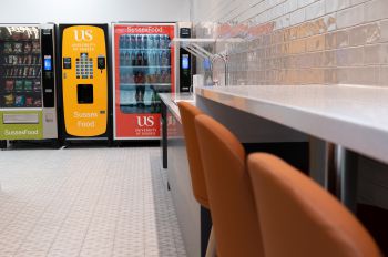 Table with high chairs along the right wall and three vending machines at the end of the room.