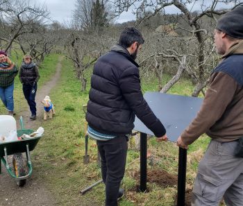 Two men installing a sign in Stanmer Park while two women and a dog walk towards