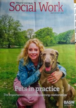 A smiling Rebecca kneels on grass with her right arm around a seated weimaraner on the cover of the latest edition of the journal 'Professional Social Work'