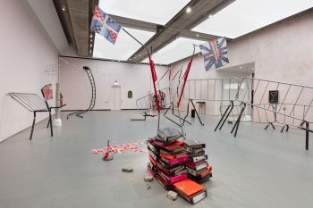 Jesse Darling's exhibition, with crowd control barriers, British flags, ring binders and hazard tape arranged haphazardly around a room