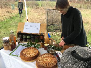 Daphne Lambert slices a beautiful nettle & rye loaf at the back of a table covered in mouth-watering looking produce.