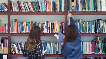 Two students browse books in the library