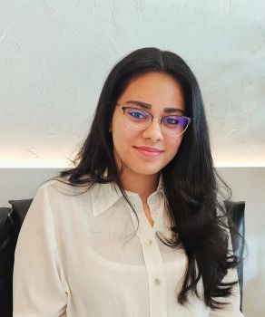 A portrait photo of a student with long, dark hair wearing glasses in front of a white background.