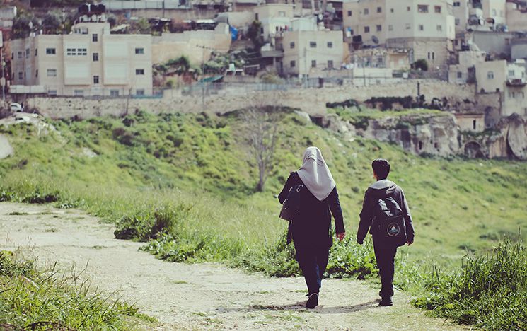 A woman and child walk along a path towards a Palestinian refugee settlement