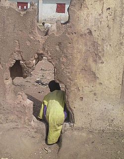 Local schoolboy climbing through hole in wall away from camera
