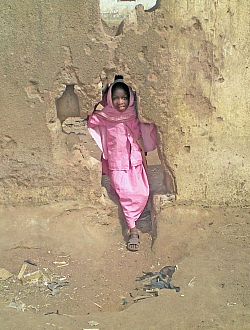 Local schoolgirl climbing through hole in wall toward camera