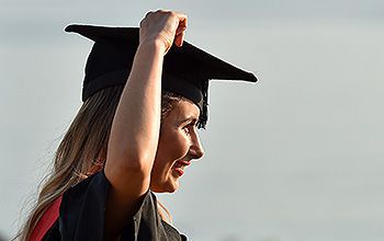 A student in a gown puts her mortar board hat on her head
