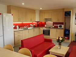 Kitchen in view. Red sofas, wooden units. Flowers on coffee table