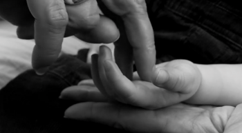 A picture of an adult's hand, with one finger touching the palm of an infant's hand
