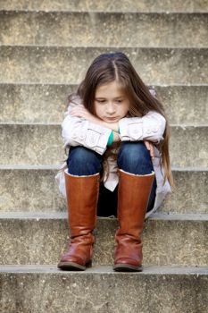 A picture of a child sitting on some stairs, looking sad