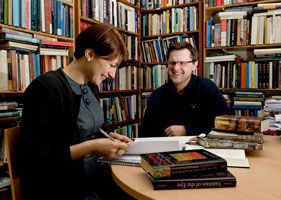 A photo of two people talking in a room where the walls are lined with bookshelves