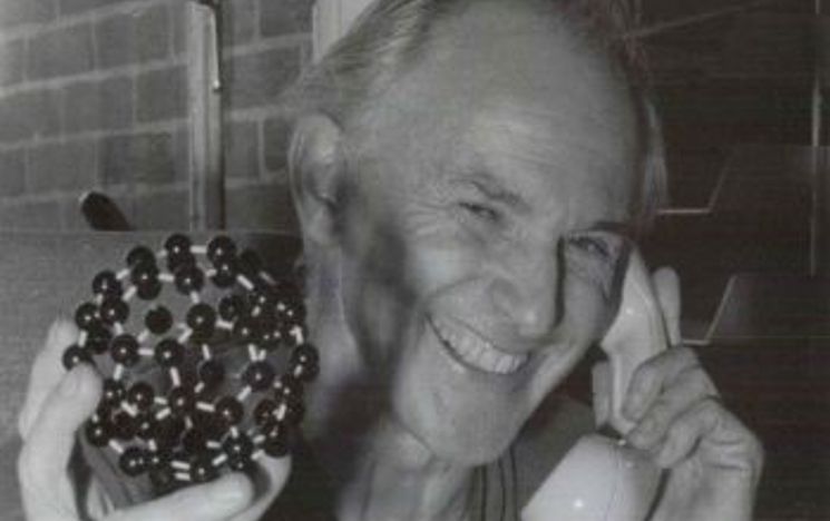 Sir Harry Kroto holding a model of a Buckyball whilst talking on the telephone.
