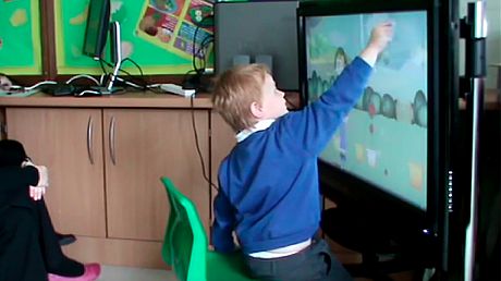 An autistic red hair child is touching a screen.