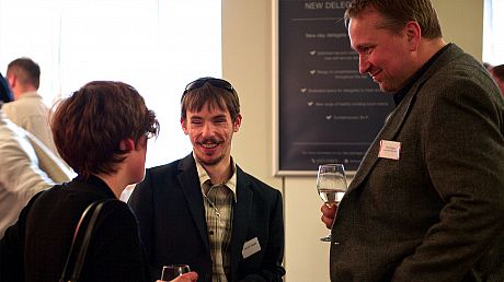 Picture of three people talking with a drink in hand.