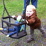 A boy pushes a stuff frog on a swing at the park.