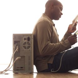 man leaning on computer reading manual