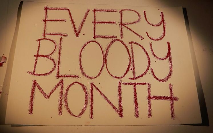 A piece of cardboard with 'every bloody month' written on in red capital letters