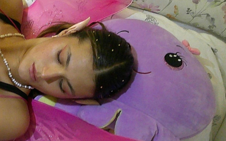 A picture of a white feminine-presenting person resting their head on a purple pillow
