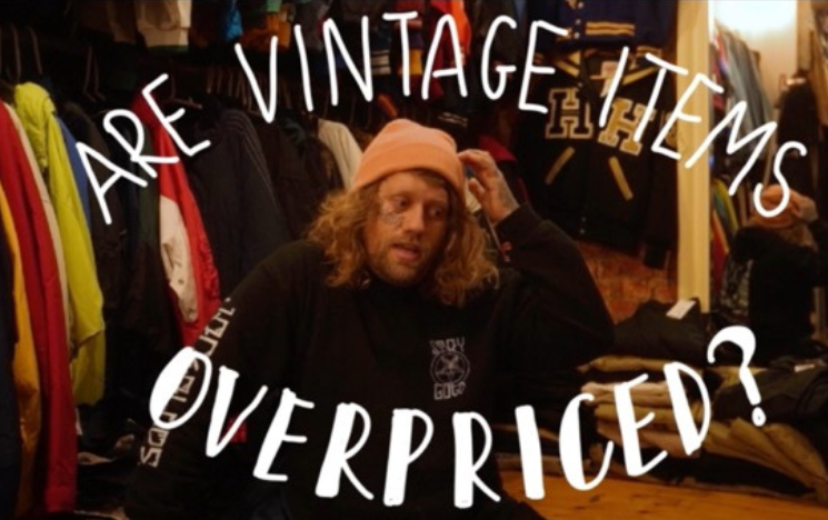 A masculine-presenting individual sitting with clothes displayed around them with the title ‘Are Vintage Items Overpriced?‘