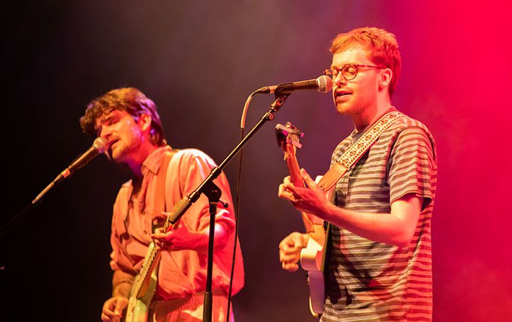 Two white males singing and playing guitars on a stage.