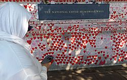A unanimous woman with her head covered stands by the National Covid Memorial Wall