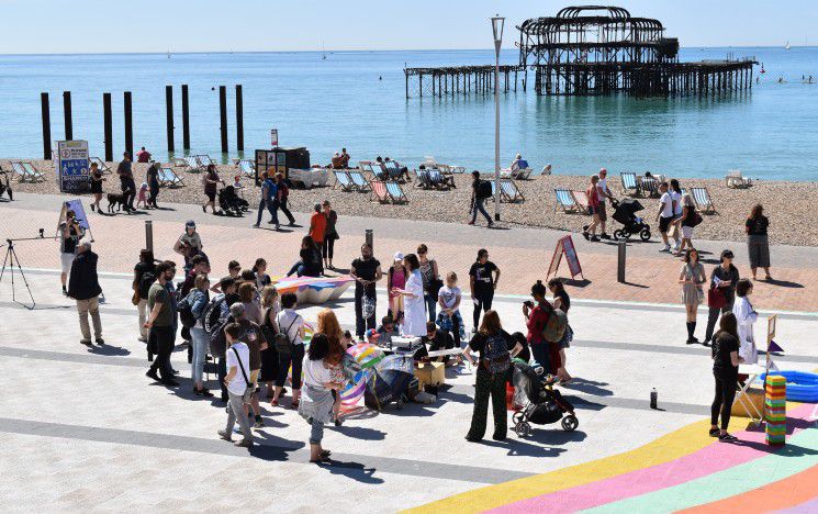 A crowd of people listening to a scientist in a lab coat in front of the West Pier in Brighton