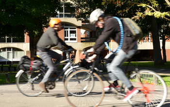 Two cyclists breezing through the University of Sussex campus on a sunny day
