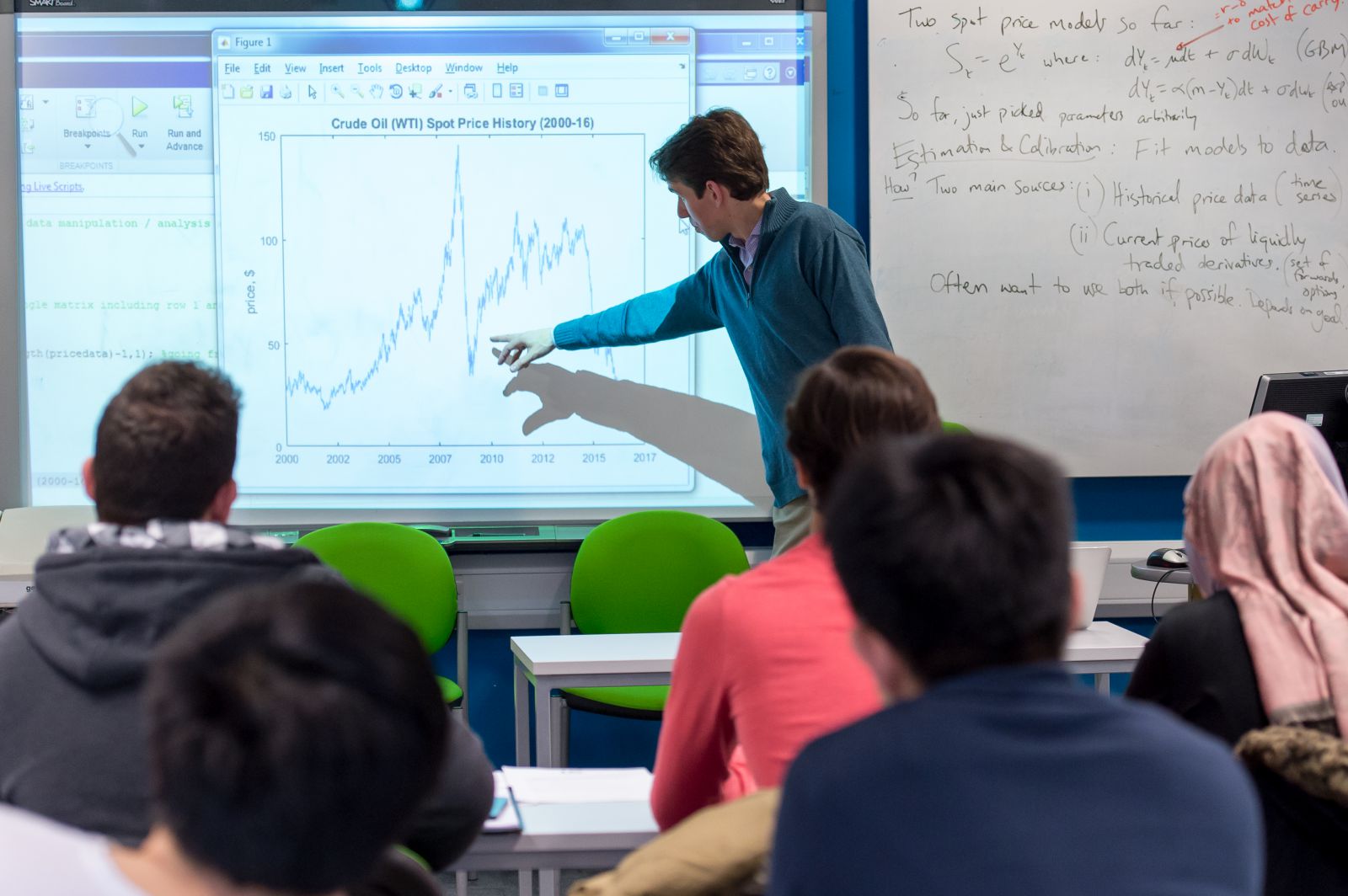 Male lecturer infront of a smartboard teaching to a class about finance