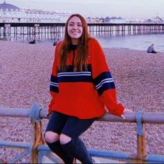 Georgina, a student graduate, sitting on the rail infront of Brighton pier