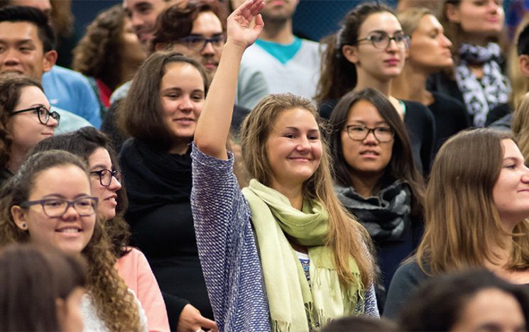 student in lecture with hand up smiling