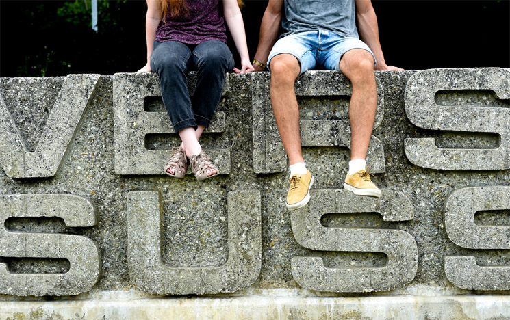 Two students sitting on the University of Sussex sign