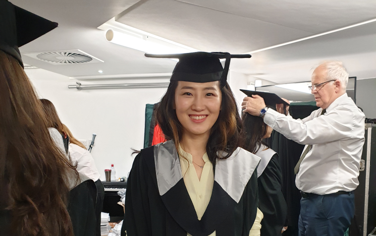 Student smiling indoors in graduation robes on graduation day