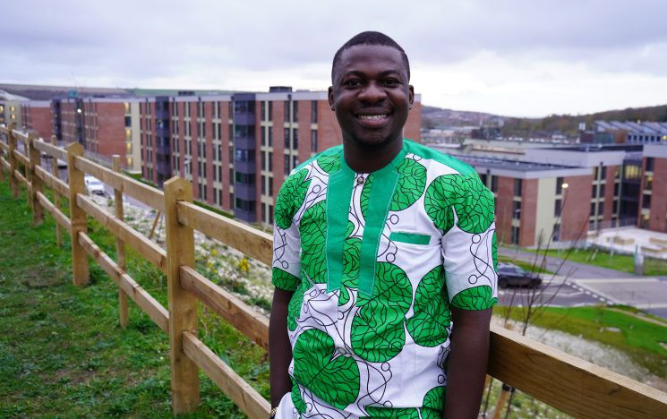 An international student ambassador stands smiling outside in front of campus accommodation on a cloudy day