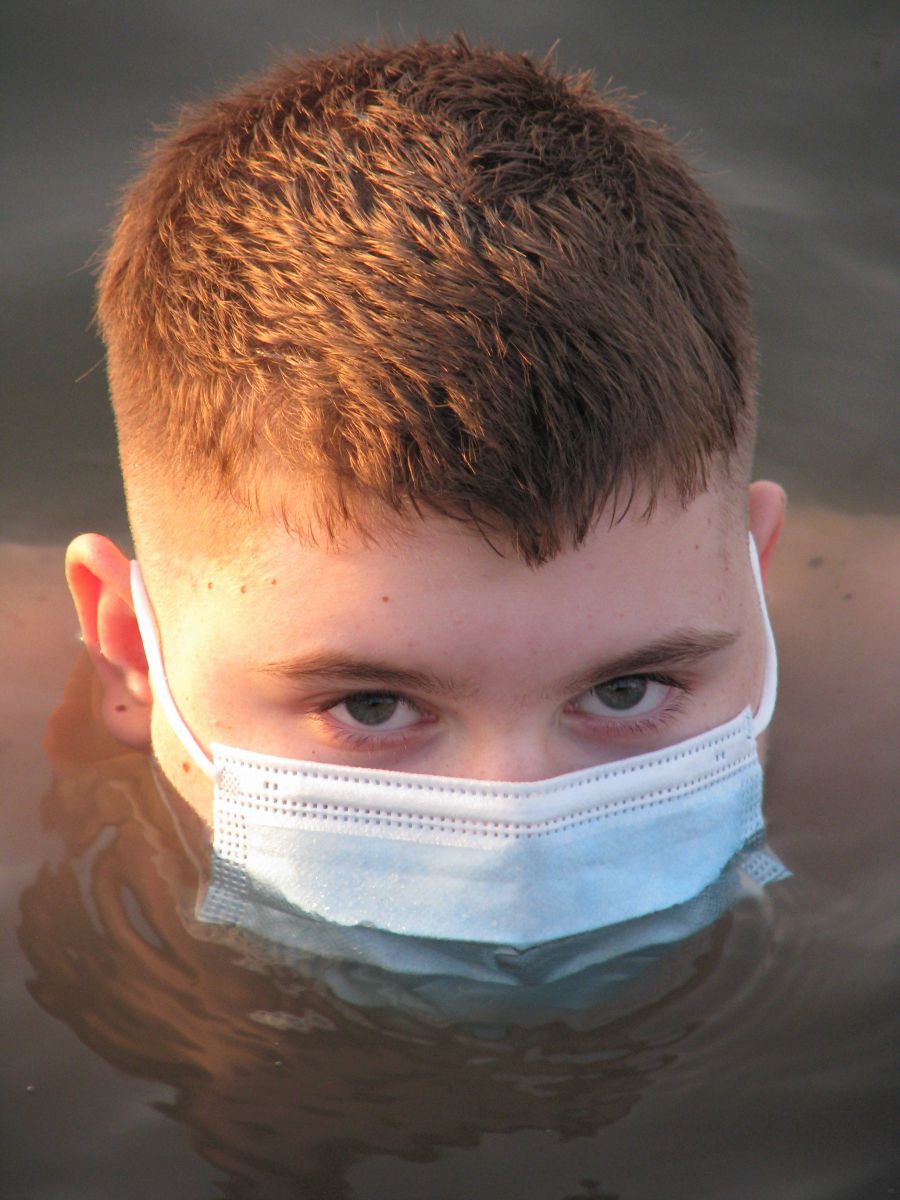 

A young man wearing a blue face mask is immersed up to his nose in murky water