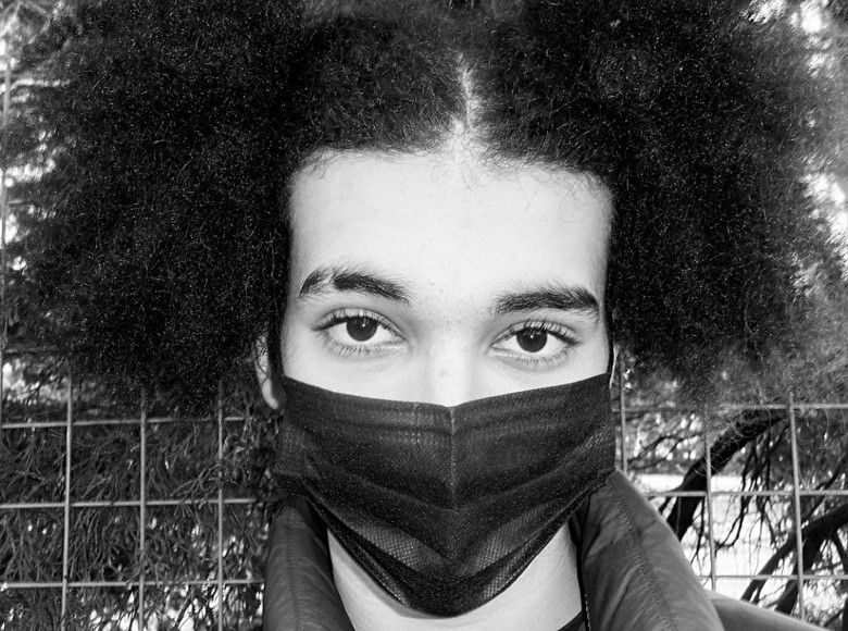 

A black and white close up photo of a young person looking into the camera up against railings