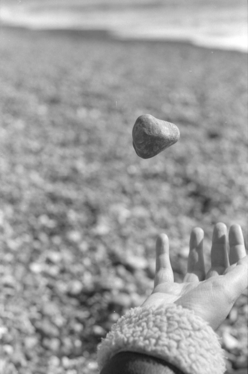 A greyscale photo of a stone being thrown up in the air in front of a beach