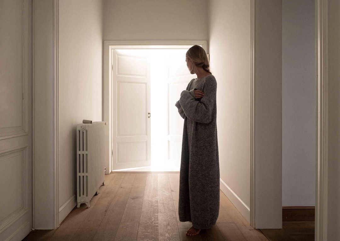 
A girl standing in a gown looks out into an open door with a bright light coming through