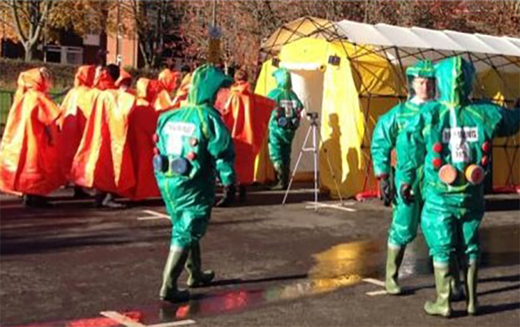 A decontamination tent with emergency services guiding people through it