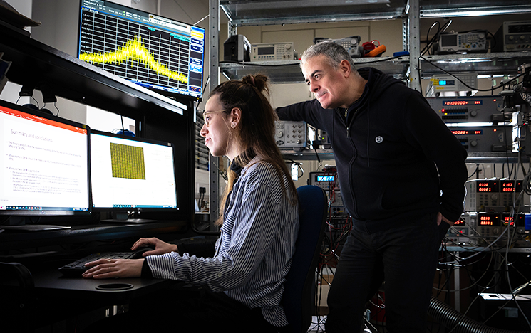 A student working at a computer in the quantum lab. A lecturer looks over their shoulder