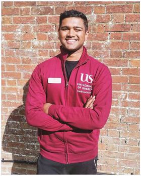 Adarsh Ramdawor standing in front of a Sussex building wearing his red Residential Adviser hoodie