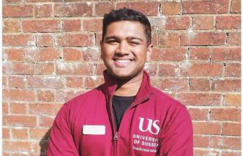 Adarsh Ramdawor standing in front of a Sussex building wearing his red Residential Adviser hoodie