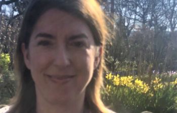 University of Sussex researcher Cassandra Wiener smiles at the camera with spring daffodils behind her