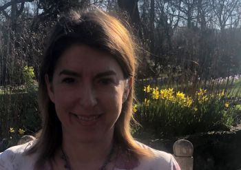 University of Sussex researcher Cassandra Wiener smiles at the camera with spring daffodils behind her